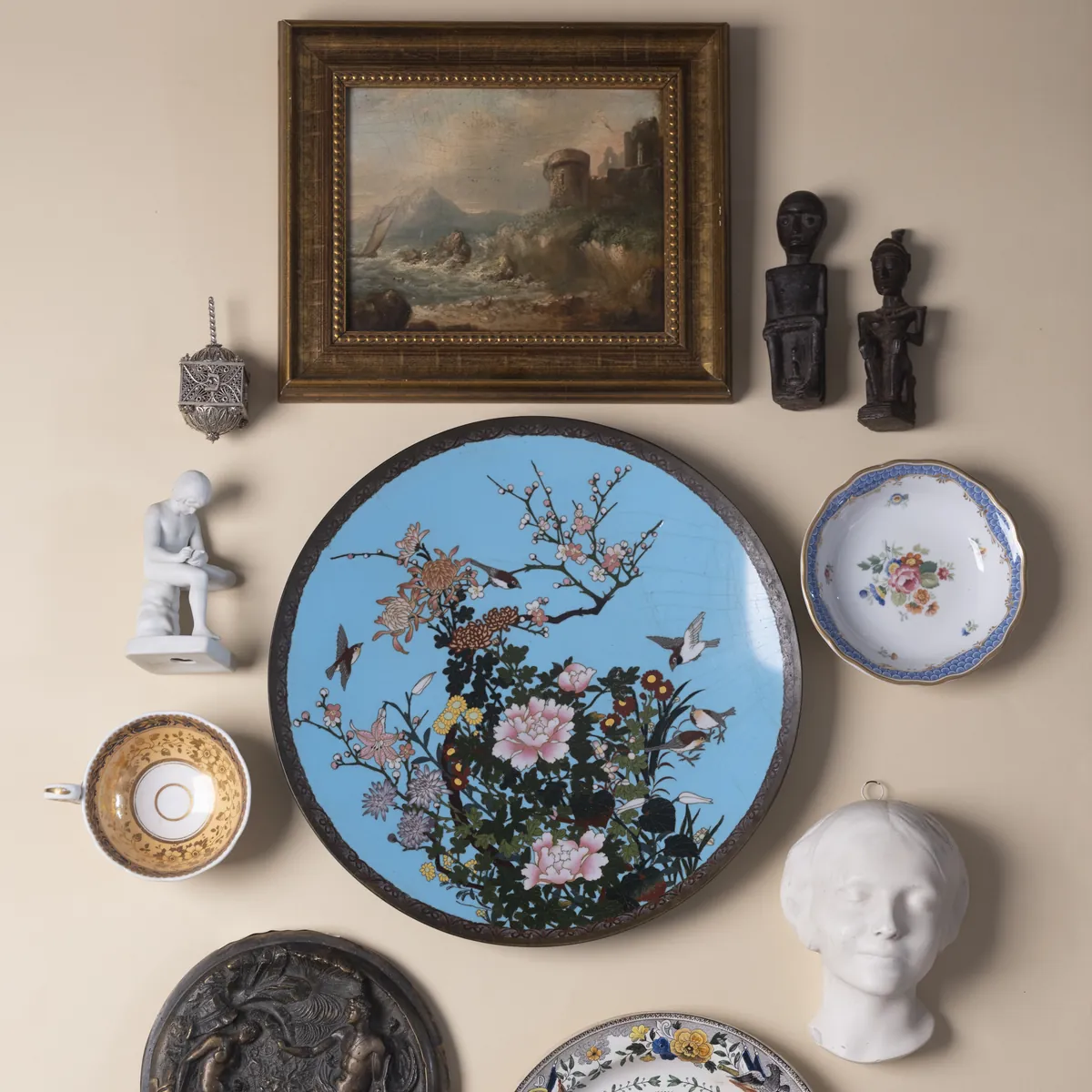 Decorative plates, masks and a framed painting arranged on a wall. Photograph by STAS PRO